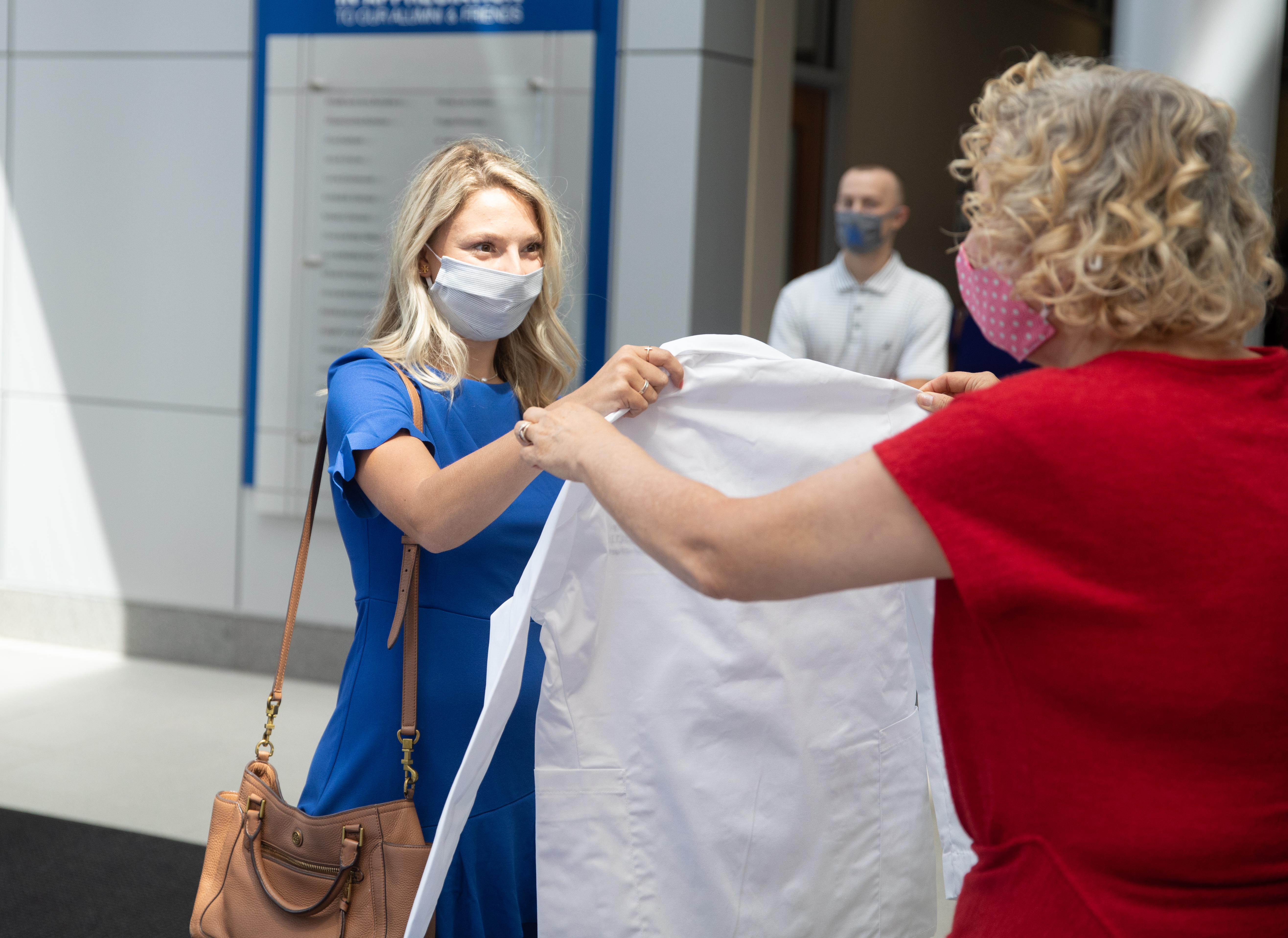 student in mask receiving white coat