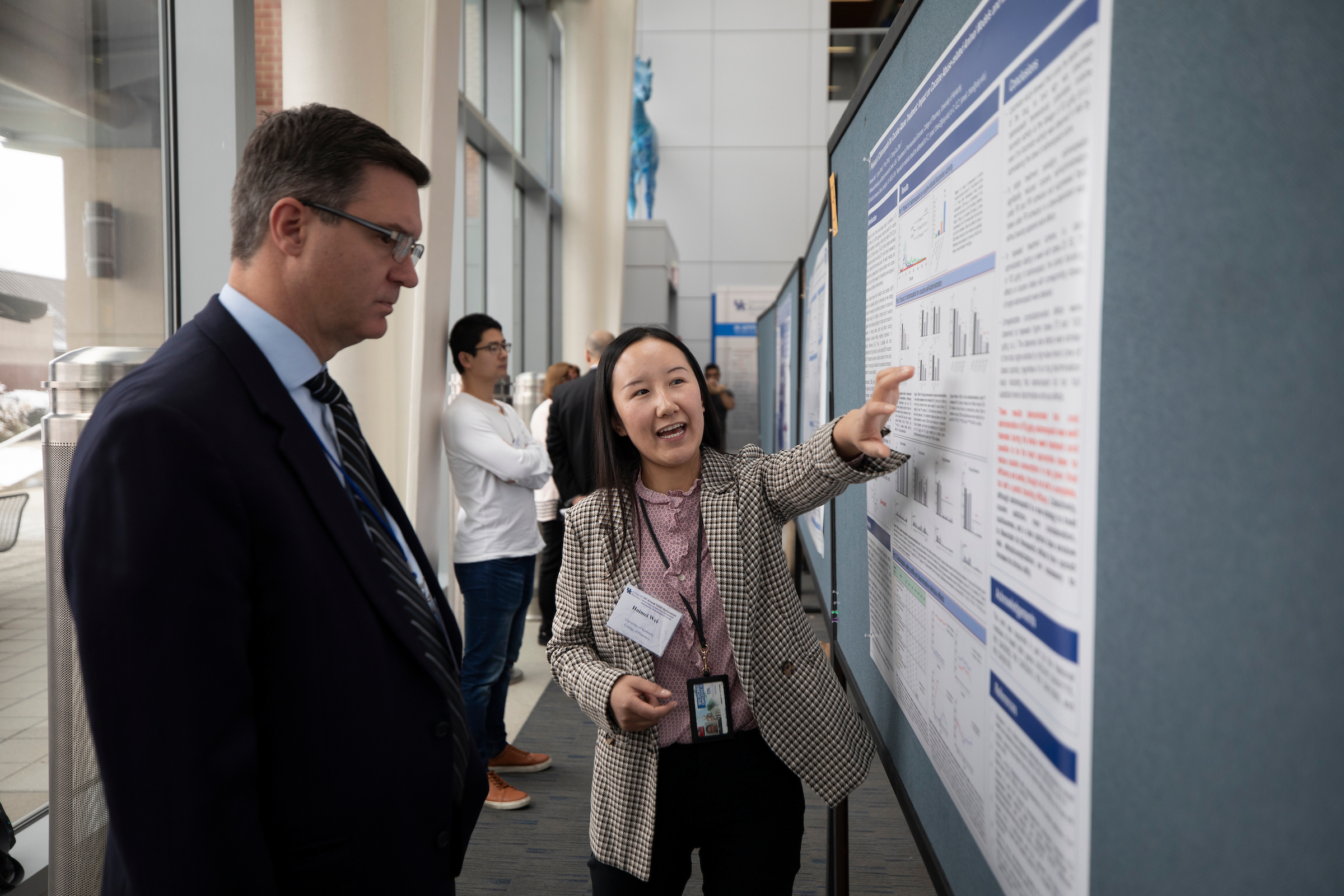 Student points to research poster while a man looks on