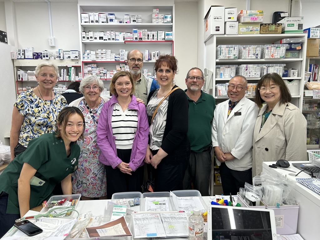 UK College of Pharmacy alumni and faculty visit a Japanese community pharmacy, posing with local pharmacists in front of shelves stocked with medicines and supplies.