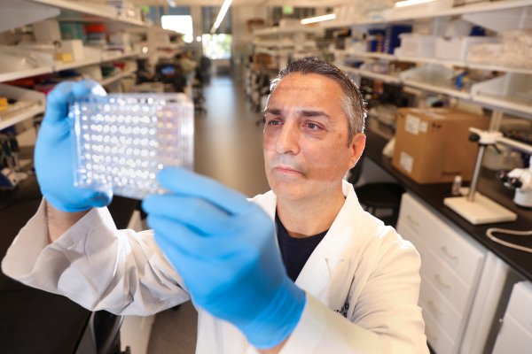 A man in white coat and lab gloves observes equipment held up to the light