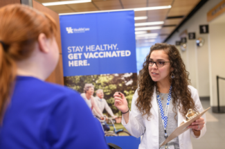 pharmacist standing in front of vaccination sign holding clipboard