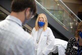 pharmacist in blue mask smiling while wearing white coat