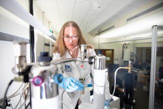 Woman standing in white coat on near top of NMR machine