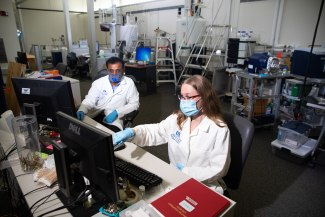 two people in masks looking at a computer near NMR machines