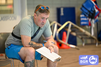 man holding a clipboard keeps track of laps at a pool