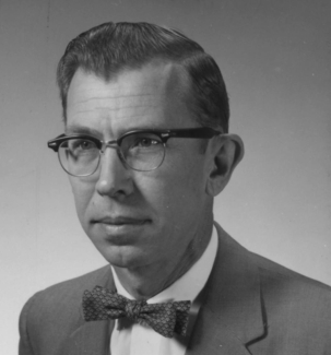 A black and white photo of a man wearing glasses and a suite with a bowtie
