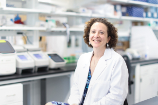 Woman in a white coat smiling in a lab setting