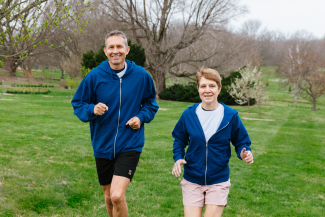 A man and a woman in matching blue hoodies run outside in a nature setting