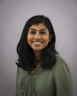 A dark haired woman in a green shirt smiles in front of a neutral background