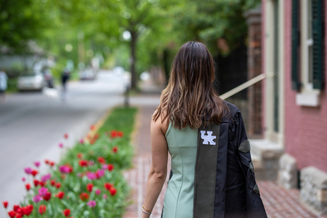 A woman walking away with a graduation robe draped over her arm