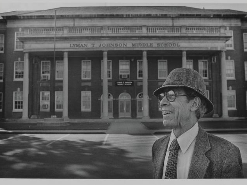 Lyman T Johnson wearing a suite, hat and glasses posing in front of Lyman T. Johnson Middle School