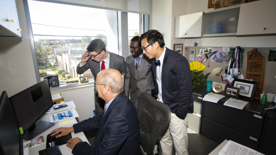 faculty member and three students looking at a computer