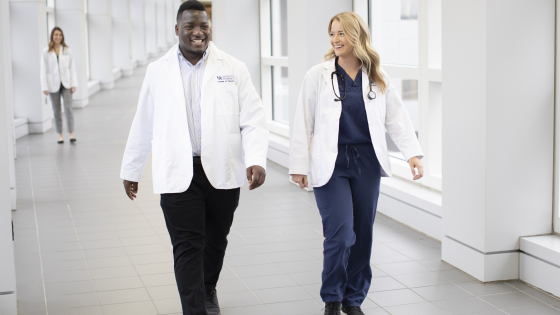 pharmacy students in white coats and scrubs smiling and walking