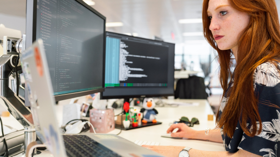 woman looking at laptop with two larger screens