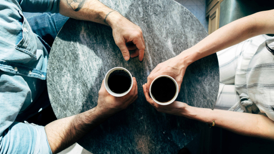 overhead view of two black cups of coffee with hands holding each cup