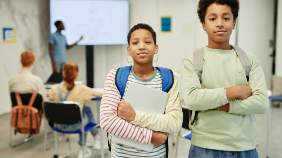 two boys with crossed arms looking at the camera while a lecture goes on in the back