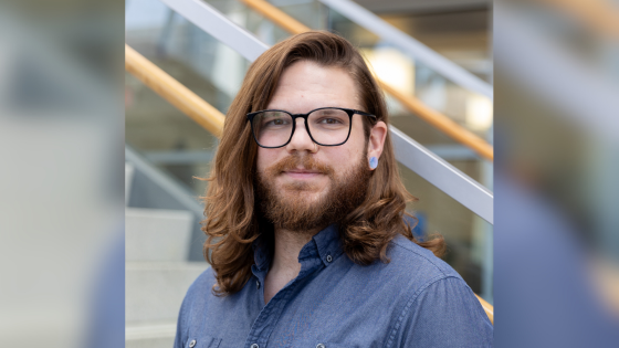 Man with shoulder length hair and black rimmed glasses smiling with closed lips