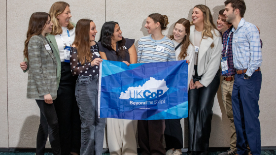 A group of young alumni holding a flag and smiling at one another