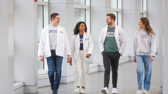 Four students wearing white coats walk down a well-lit hallway