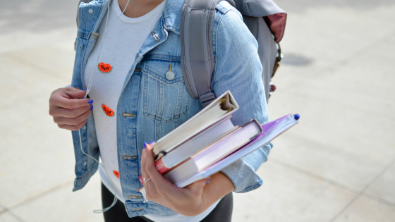 a person wearing a backpack and holding a stack of books and binders
