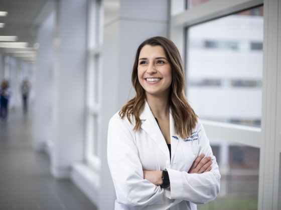 female pharmacy student  in white coat, smiling in pedway with arms crossed