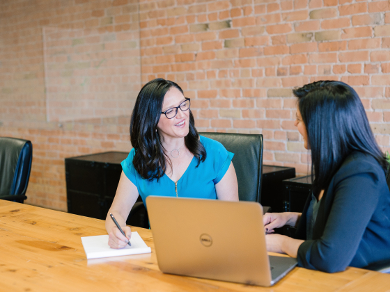 two women at a table with a computer and notepad