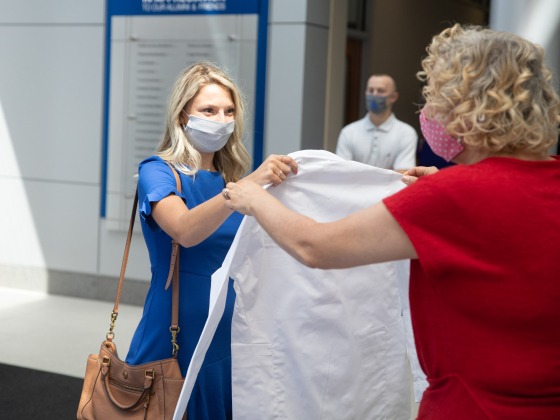 student in mask receiving white coat