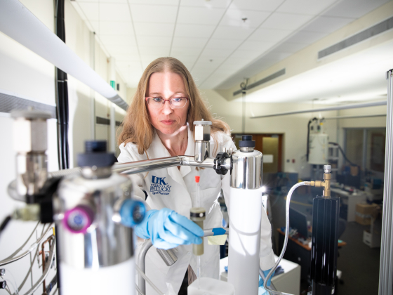 Woman standing in white coat on near top of NMR machine