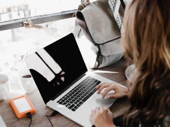 brown-haired woman sitting at coffee bar with macbook and external hard drive