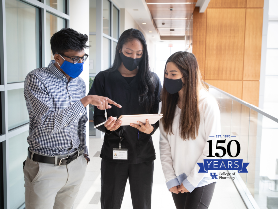 three students wearing masks looking at an iPad