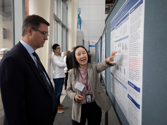 Student points to research poster while a man looks on