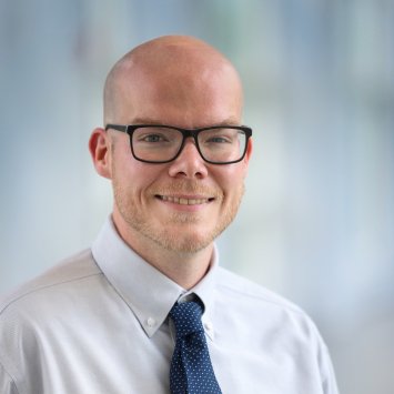 Man wearing glasses and a tie smiling