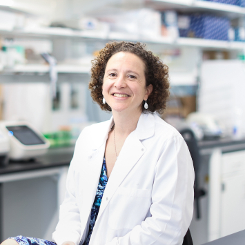 Woman in a white coat smiling in a lab setting
