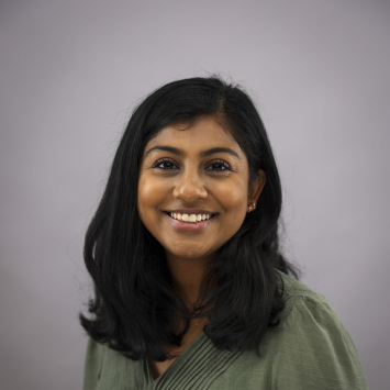 A dark haired woman in a green shirt smiles in front of a neutral background