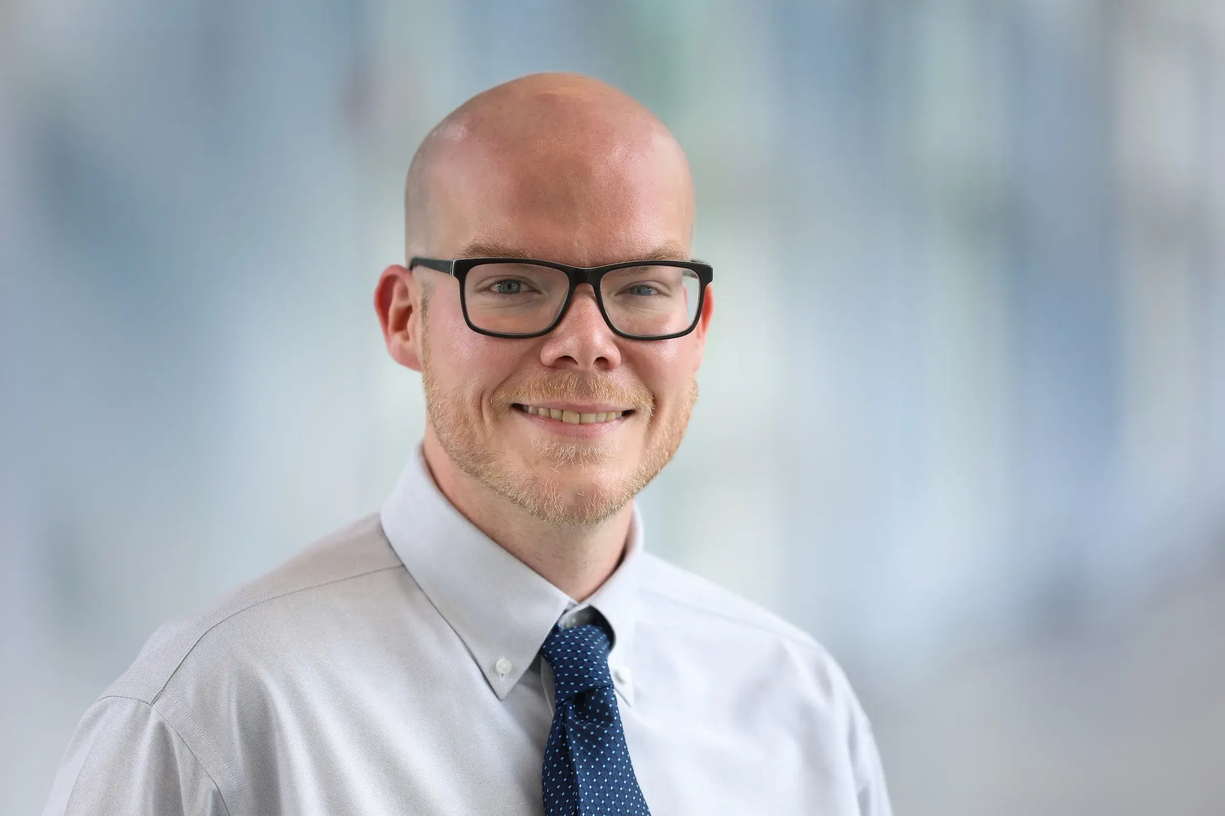 Man wearing glasses and a tie smiling