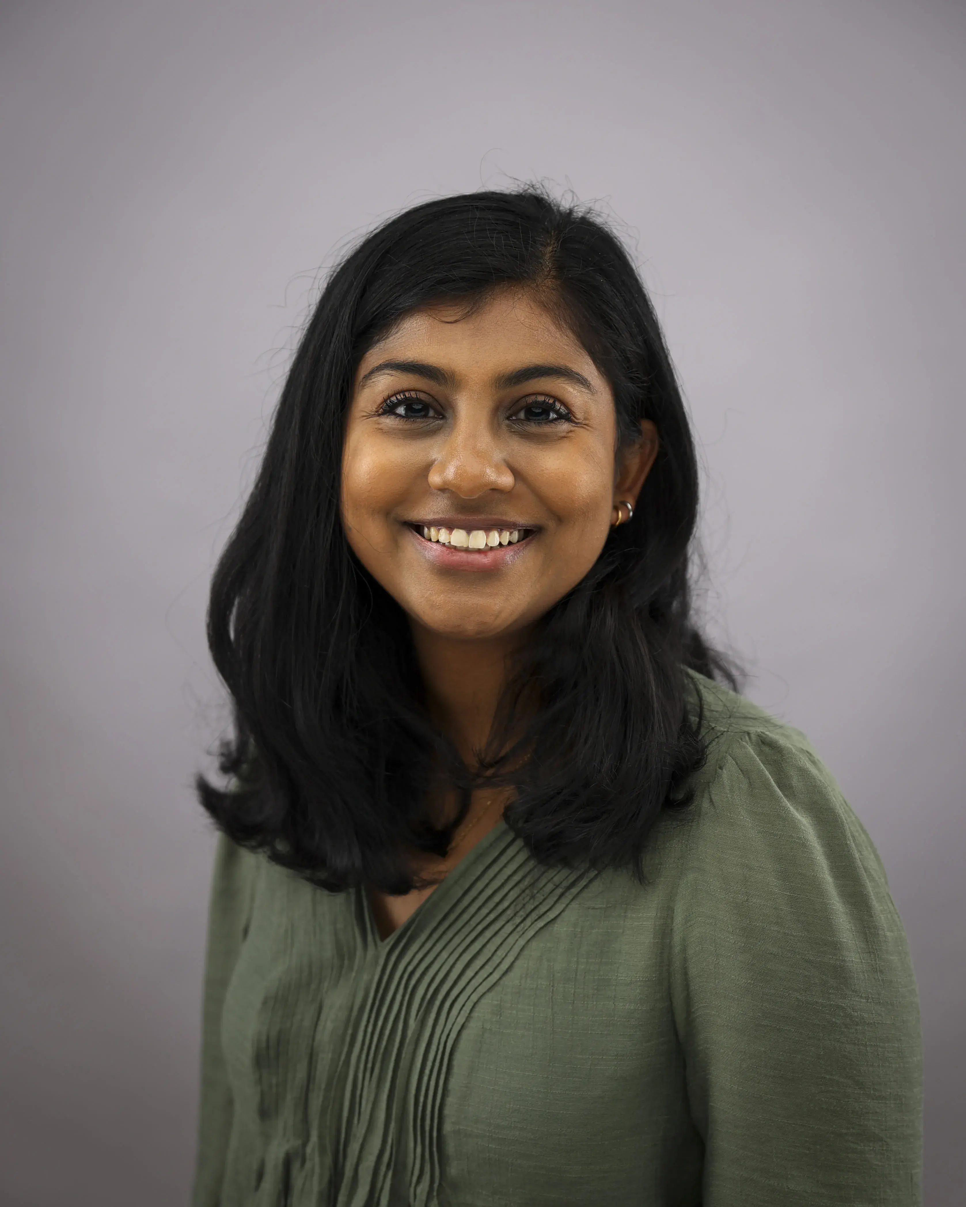 A dark haired woman in a green shirt smiles in front of a neutral background